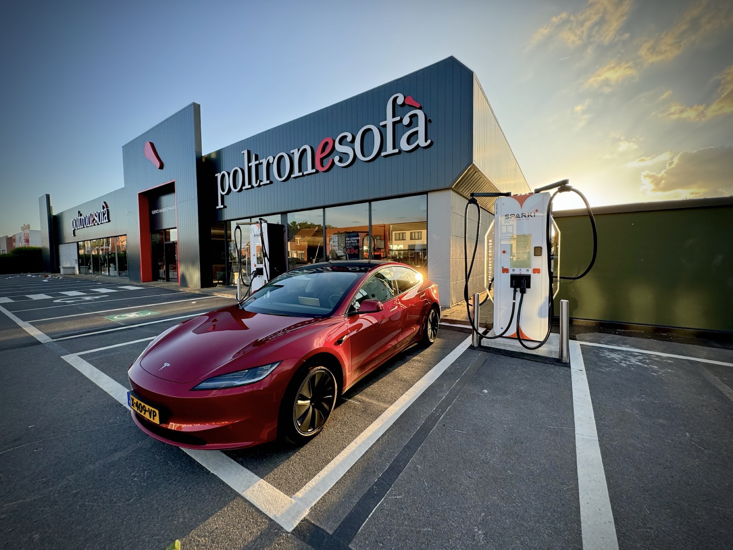 Tesla Model 3 charging at a Sparki Amber II station in a retail parking lot